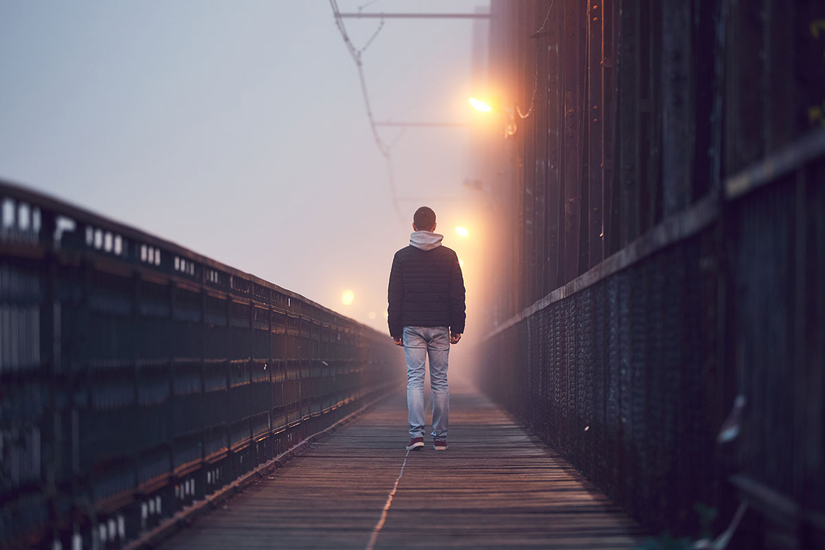 A youth walking away from the camera on a bridge.