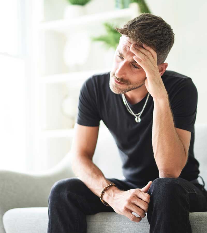 A man sitting in a chair with his head held in his hand.